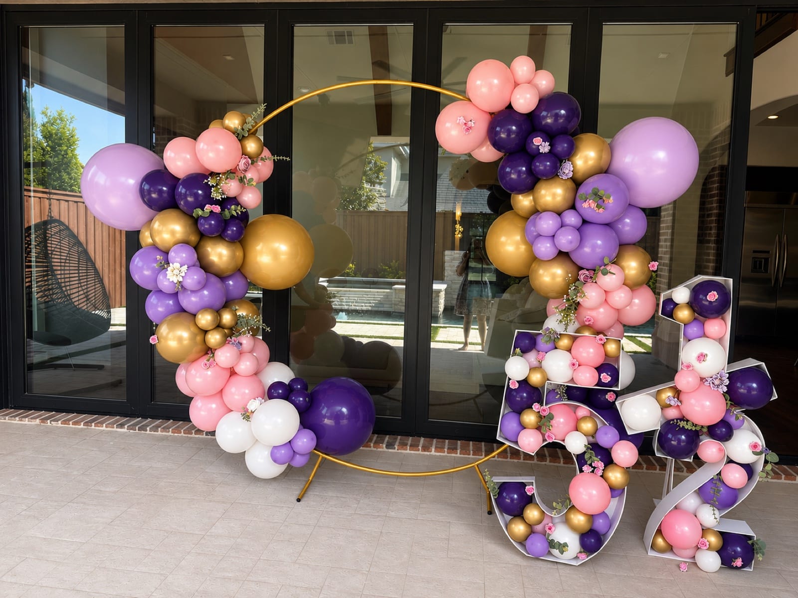 Marquee numerals packed with balloons reading five and a half, beside a gold ring wound in plum, lilac and blush