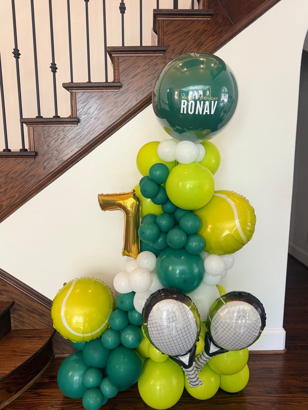 A column of lime and forest balloons hung with foil tennis rackets, tennis balls and a gold number seven